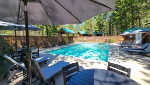 A swimming pool with lounge chairs and umbrellas, surrounded by wooden fences and trees. - Birch Room 10 - loft room at The Inn At Mazama (Mazama)