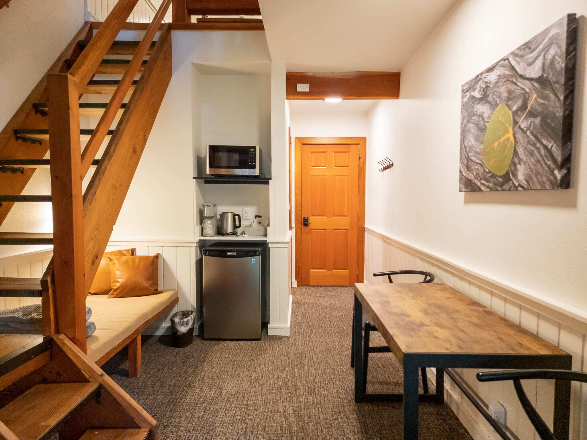 Un espacio habitable compacto con una escalera de madera, una kitchenette con microondas, un refrigerador y una mesa de comedor con sillas.