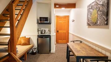 Un espacio habitable compacto con una escalera de madera, una kitchenette con microondas, un refrigerador y una mesa de comedor con sillas.