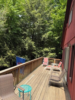 Une terrasse en bois, agréée de mobilier dâextĂ©rieur, entourĂ©e dâarbres denses.