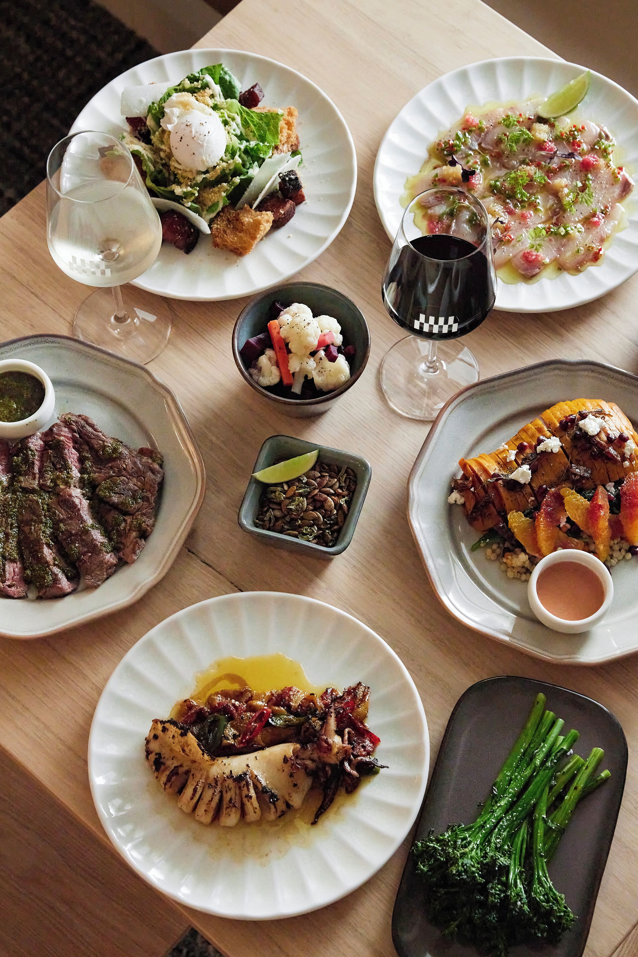 A table with various dishes, including steak, salad, and seafood, along with glasses of wine.