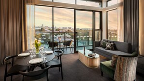 A modern hotel room with a dining area, a sofa, and a large window offering a city view. - Majestic M Suites (North Adelaide)