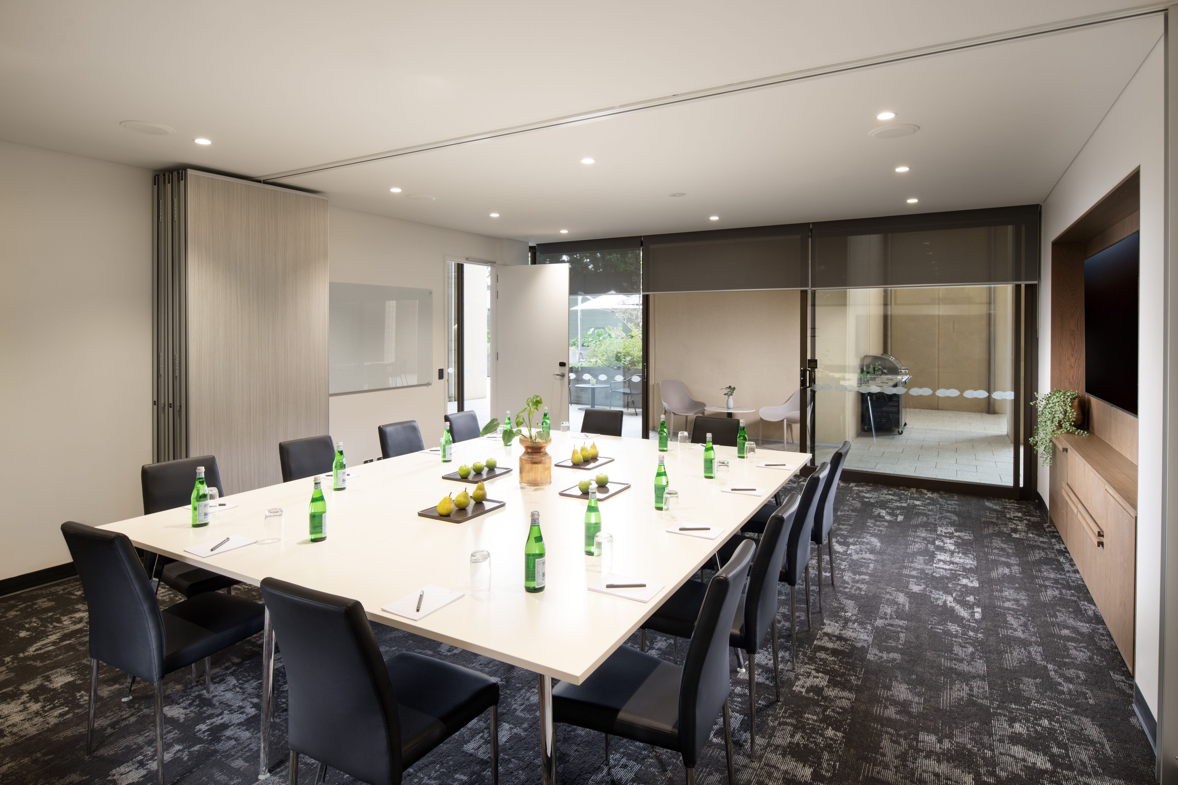 A conference room with a long table, black chairs, and green bottles.