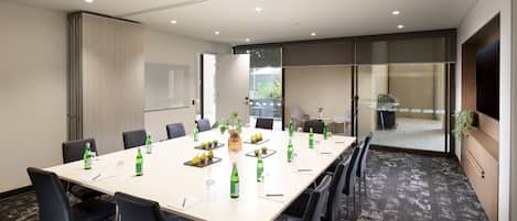 A conference room with a long table, black chairs, and green bottles.