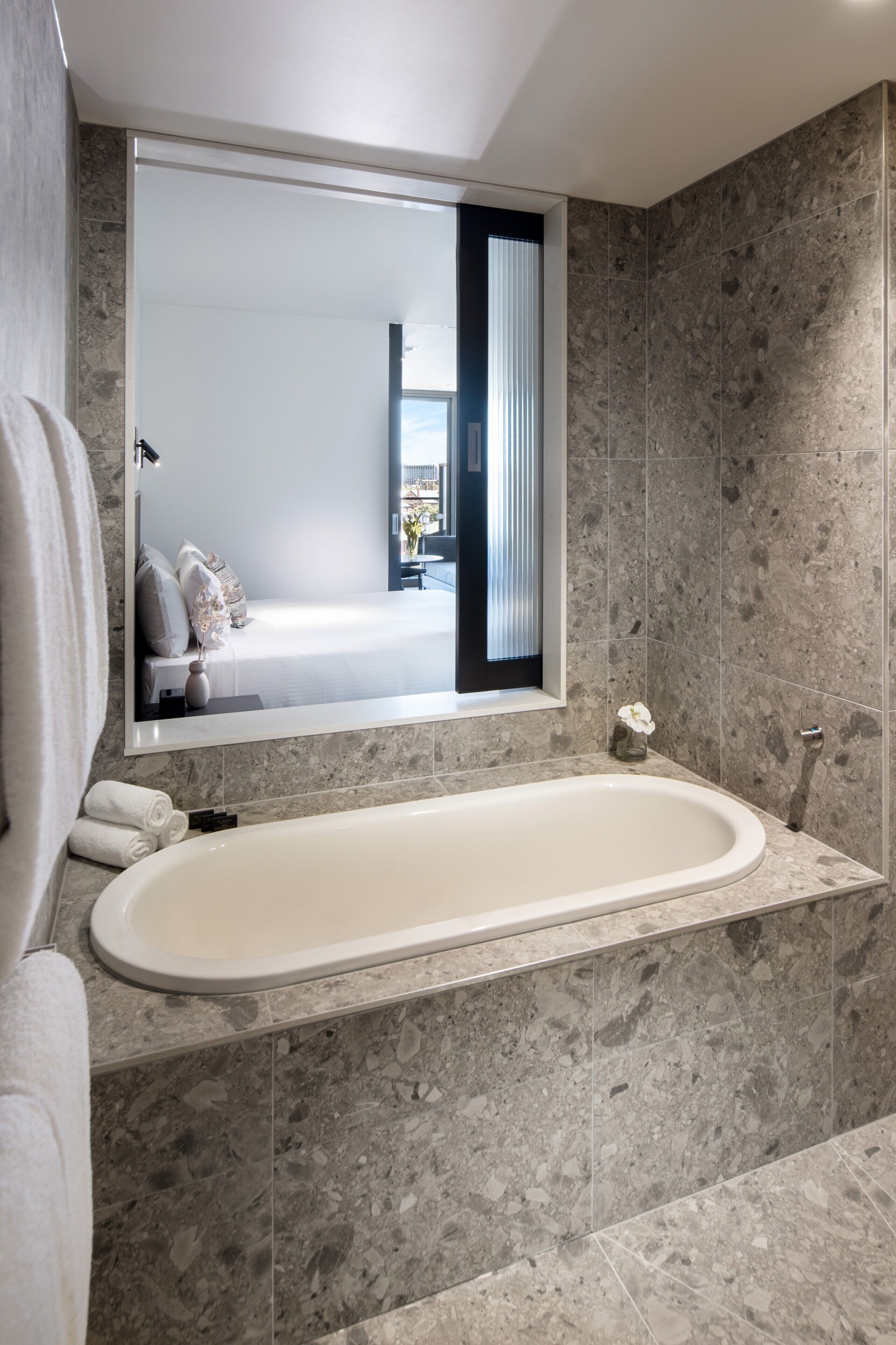 Een moderne badkamer met een vrijstaand bad, een grote spiegel en een betegelde wand van marmer.