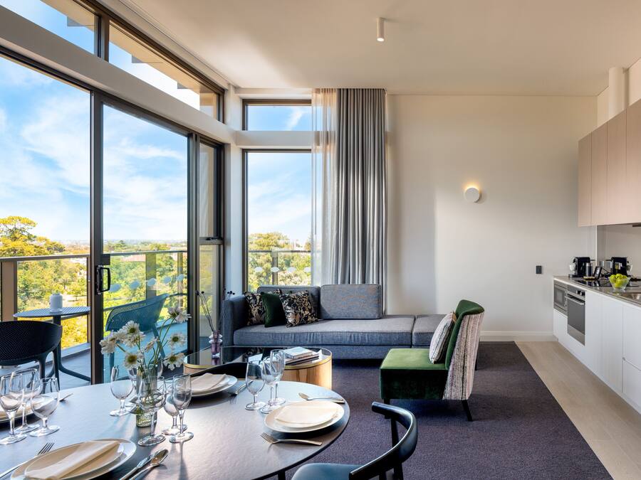 A modern kitchen with a dining area, large windows, and a view of the outdoors.