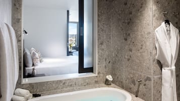 A modern bathroom with a freestanding bathtub, a large mirror, and a robe hanging on a rack.