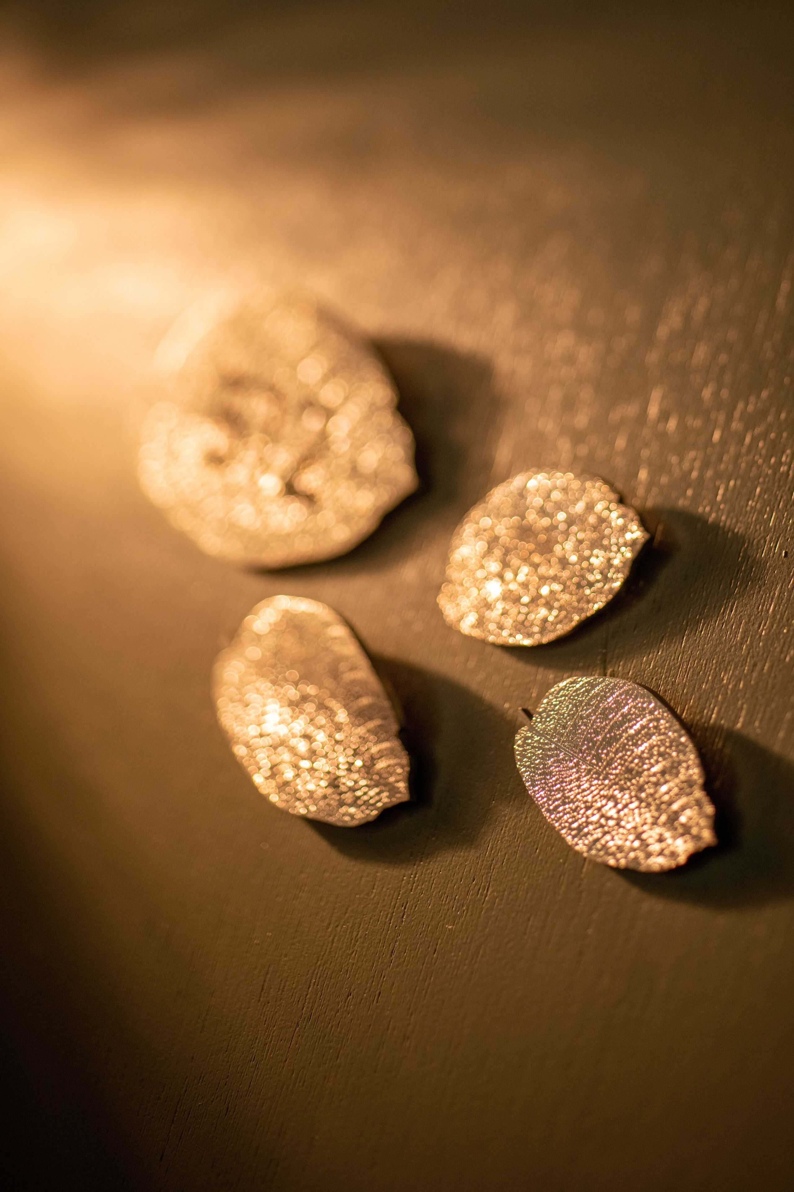 Four metallic, leaf-shaped objects on a dark surface.