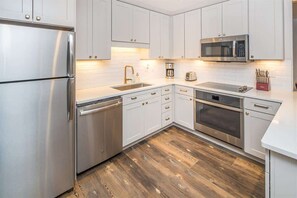 A modern kitchen with white cabinets, stainless steel appliances, and a wooden floor.