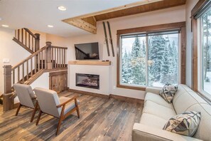 Ein gemütliches Wohnzimmer mit einer Holztreppe, einem Kamin und einem großen Fenster mit Blick auf Schnee.