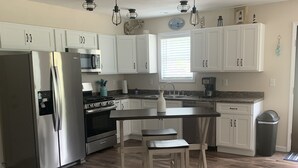 A modern kitchen with white cabinets, stainless steel appliances, and a wooden dining table. - "NEWLY BUILT" 3 Bedroom /2Bath House on the Lake (Benton)