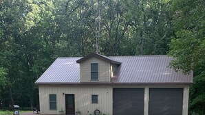 A two-story house with a metal roof, a front porch, and a driveway leading to a garage. - "NEWLY BUILT" 3 Bedroom /2Bath House on the Lake (Benton)