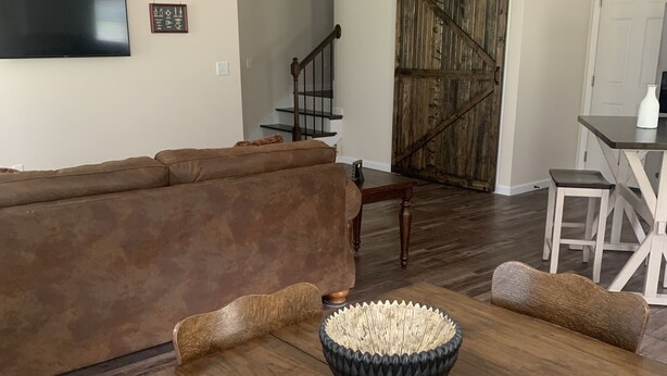 A spacious living room with a wooden dining table, a brown leather couch, and a large wooden door. - "NEWLY BUILT" 3 Bedroom /2Bath House on the Lake (Benton)