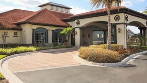 A two-story building with a red-tiled roof, a covered entrance with arches, and a landscaped driveway. - Ref 432. Stunning Villa at Bella Vida Resort near Disney. (Kissimmee)