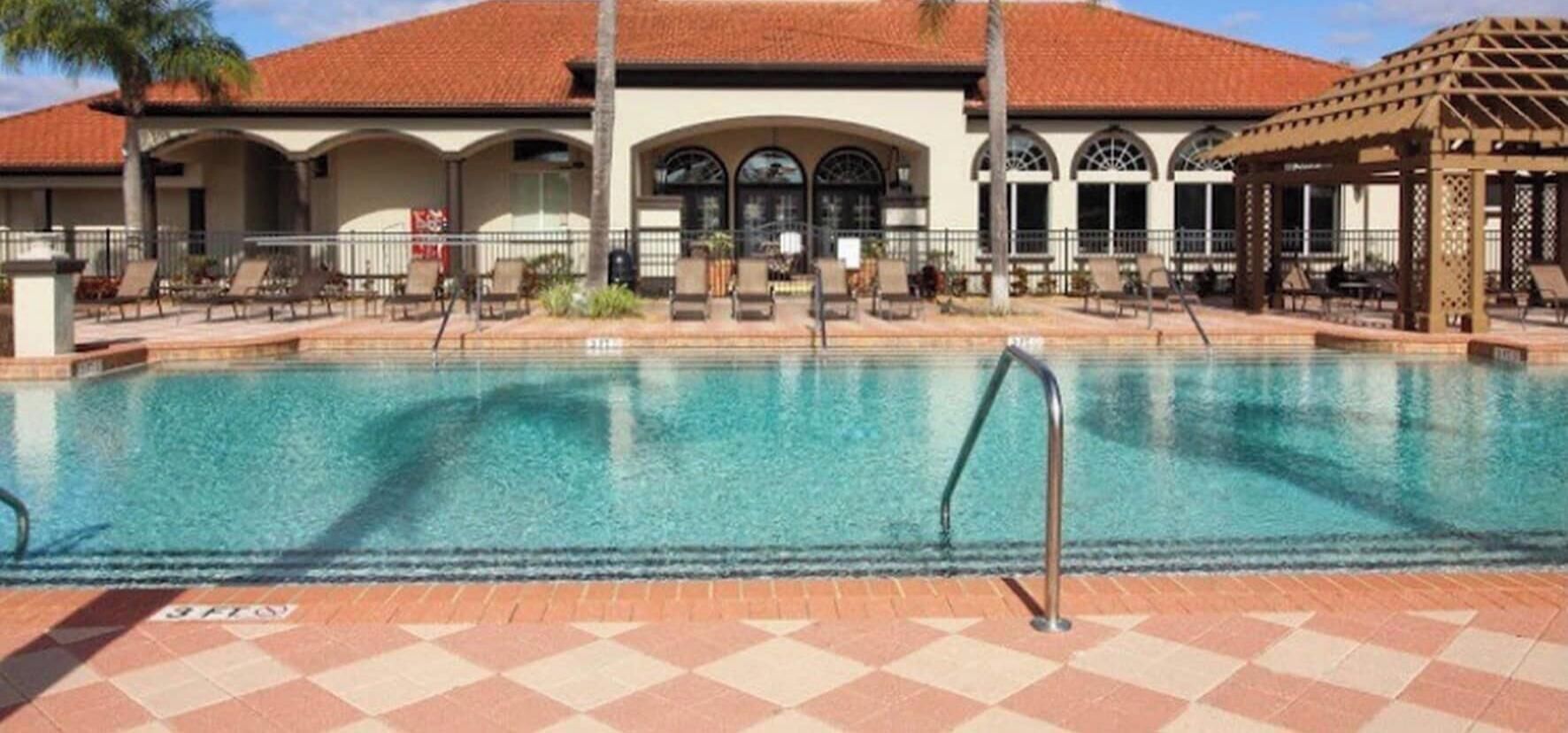 Une piscine dotée d’une terrasse carrelée, de chaises longues et d’un espace abrité agrémenté d’une pergola.