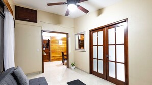 A living room with a sofa, a ceiling fan, a wooden door, and a hallway leading to another room. - In the middle of the best beaches, private house with pool. (Tamarindo)