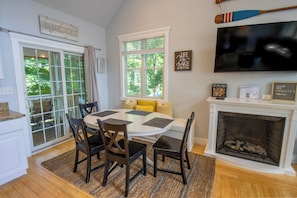 A dining room with a round table, chairs, a fireplace, and a television mounted on the wall.