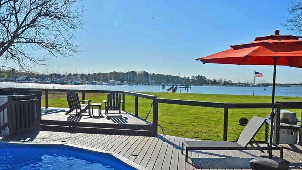 Une terrasse en bois avec une piscine, des chaises longues et un drapeau américain.