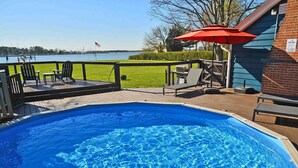 Une piscine avec une terrasse en bois, des chaises longues et un parasol.