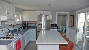 Une cuisine moderne avec des meubles blancs, un réfrigérateur en acier inoxydable, une cuisinière à gaz et un îlot en marbre agrémenté de tabourets de bar.