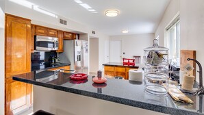 Une cuisine moderne dotée de plans de travail en granit, d’armoires en bois, d’appareils électroménagers en acier inoxydable et d’une table basse en verre.