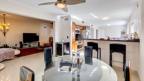 Un salon moderne avec une table à manger en verre, un téléviseur et un ventilateur de plafond.