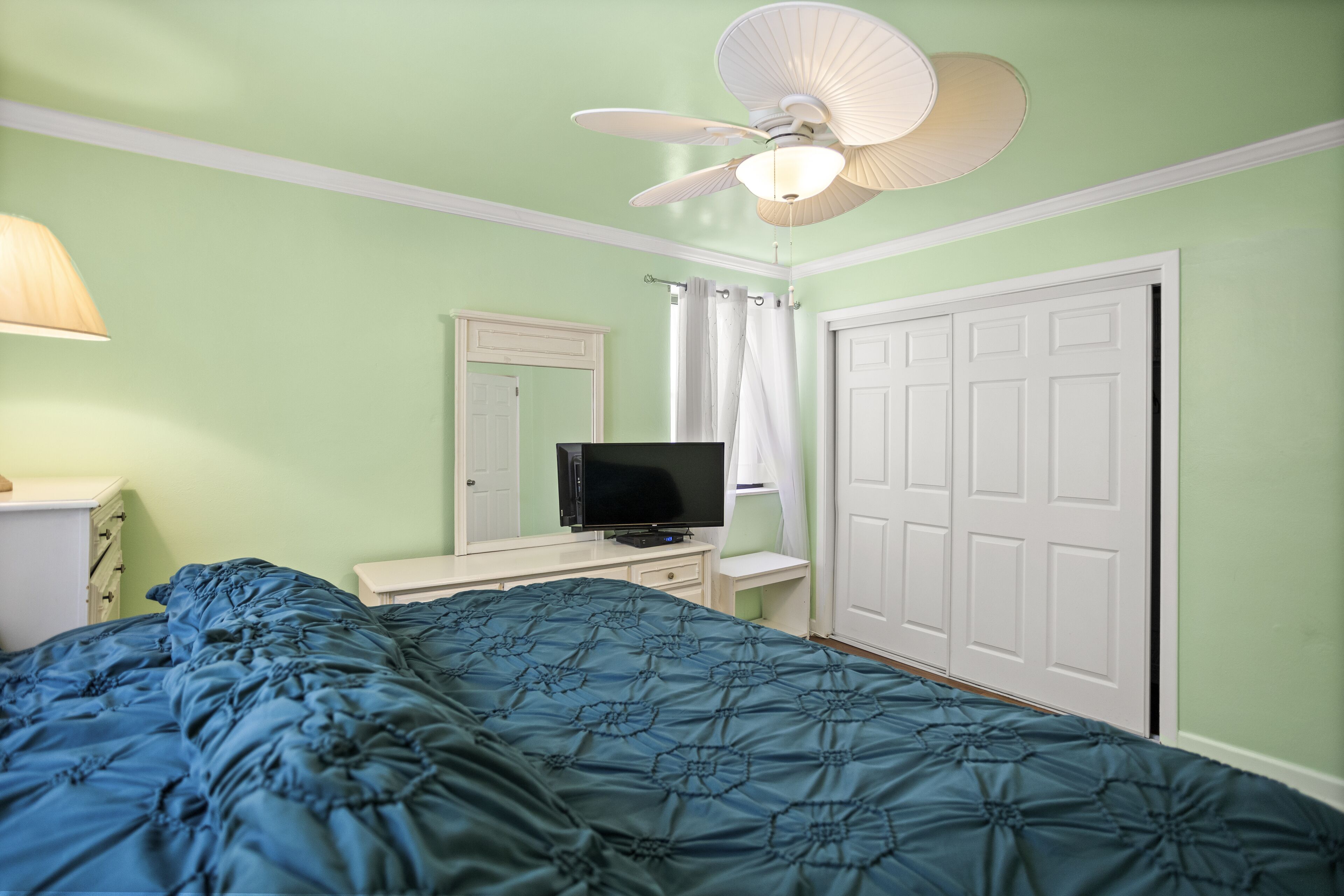 Een slaapkamer met een bed, een televisie, een plafondventilator en een kledingkast.