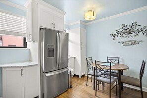 Una cocina con armarios blancos, un refrigerador de acero inoxidable, una mesa de comedor con sillas y una lámpara de pared.