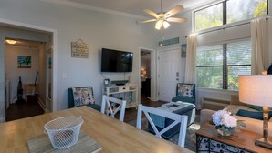 Un salon décoré sur le thème de la plage, avec un ventilateur de plafond, un téléviseur et un coin repas comprenant une table et des chaises.