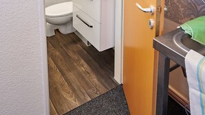 Un baño con inodoro, lavamanos y ducha. Hay un perchero sobre el lavamanos y una toalla colgada en la pared.