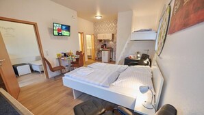 Habitación de hotel pequeña con cama, escritorio, silla, televisor y kitchenette.