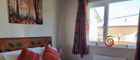 Una cama bien hecha con un cabecero floral, una ventana con vistas al exterior y un adorno en el alféizar.
