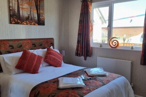 A neatly made bed with a floral headboard, a window with a view of the outside, and a decorative item on the windowsill.