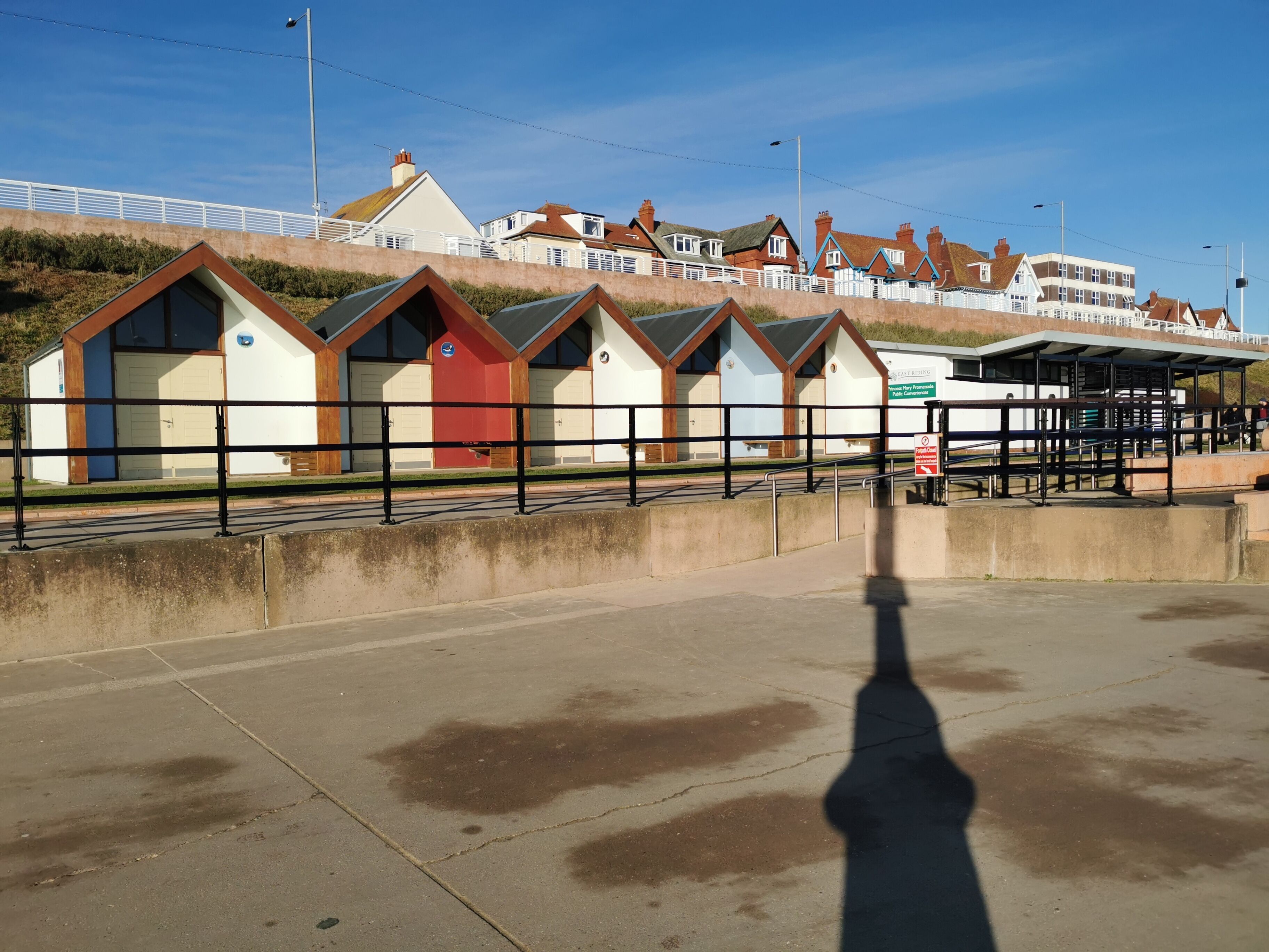 A row of beach huts with a clear view of the sea and a parking area in the foreground.