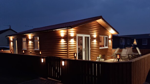 A wooden cabin with a deck, a covered patio, and a small outdoor seating area. - Captivatingly Stunning 2-bed Chalet in Bridlington (Bridlington)
