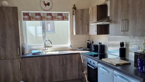 A modern kitchen with wooden cabinets, a sink, a window with curtains, a toaster, a coffee maker, and a dishwasher. - Captivatingly Stunning 2-bed Chalet in Bridlington (Bridlington)