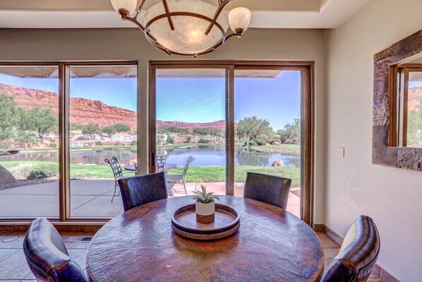 A dining area with a round table, chairs, and a view of a lake and mountains.