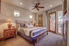 A bedroom with a bed, two bedside tables, a ceiling fan, and a view of the outside through a glass door.