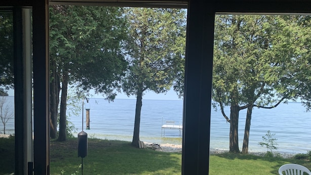 A view from a room with a wooden deck overlooking a lake, with trees and a dock visible.