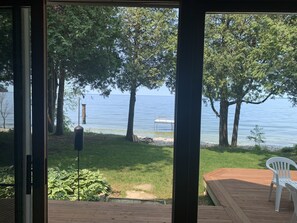 Uitzicht vanuit een kamer met een houten terras op een meer, met bomen en een steiger.