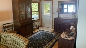 A cozy living room with a patterned sofa, a wooden cabinet with glass doors, a dining table with a vase, and a ceiling fan.