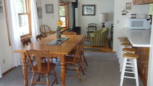 A dining area with a wooden table and chairs, a kitchen with a microwave, and a bar area with stools.