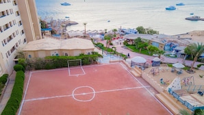A tennis court with a net, surrounded by palm trees and a pool area. - Sphinx Aqua Park Beach Resort (Hurghada)