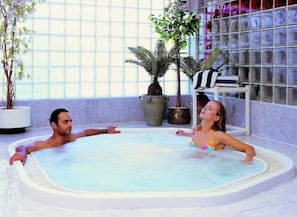 A hot tub with two people, surrounded by potted plants and a shelving unit with items. - Sphinx Aqua Park Beach Resort (Hurghada)