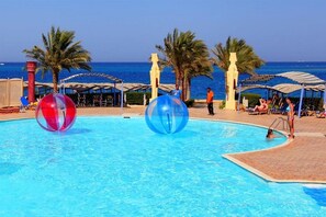 Una piscina con dos esferas transparentes grandes, palmeras y sombrillas de playa.