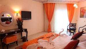 A hotel room with a bed, a desk with a chair, a television, and a large window with curtains. - Sphinx Aqua Park Beach Resort (Hurghada)