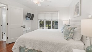 Ein Schlafzimmer mit einem Bett, einem Deckenventilator, einem Fernseher und einem Fenster mit Jalousien.
