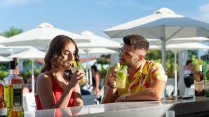 Dos personas en un bar al aire libre con sombrillas blancas, sosteniendo bebidas con lima y menta.