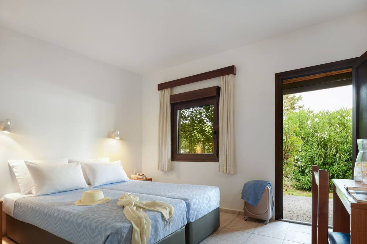 Une chambre à coucher avec un lit, des lampes de chevet, une fenêtre et une vue sur la verdure.