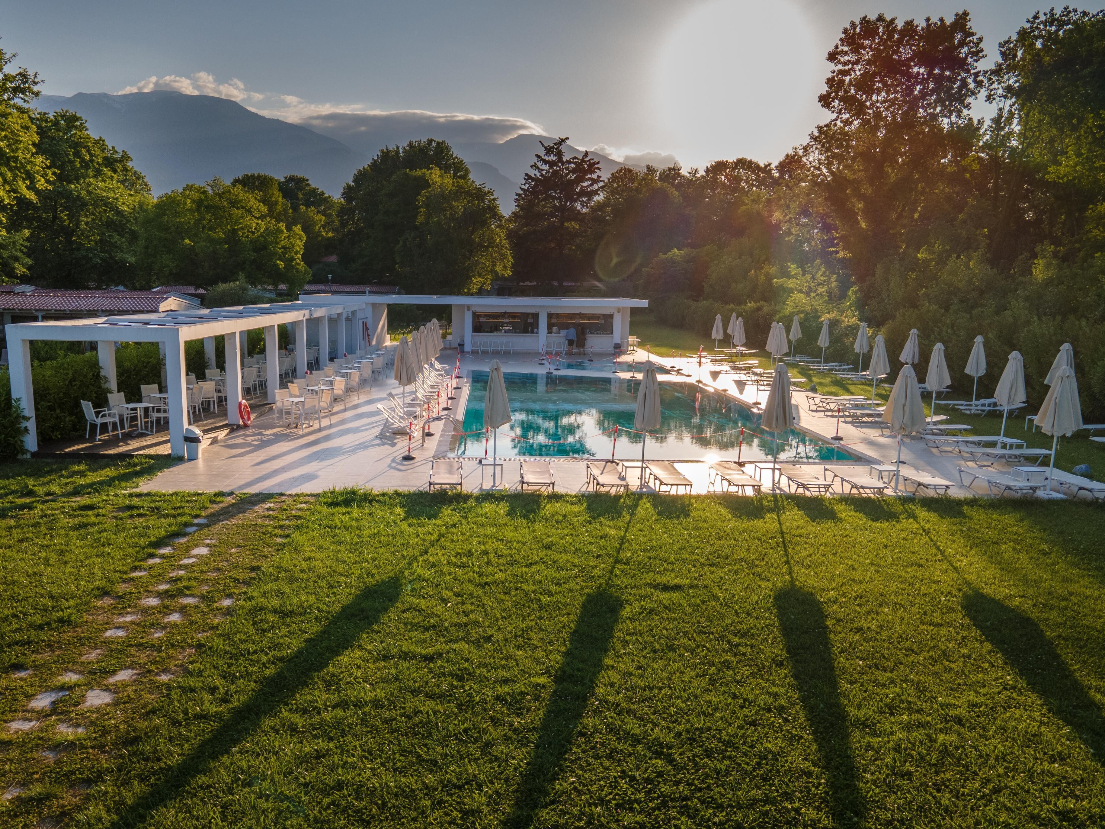 A pool area with lounge chairs and umbrellas, surrounded by a covered seating area and a building with a terrace.